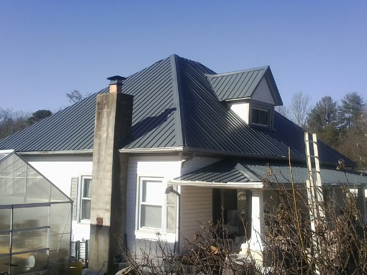 Dark blue standing seam metal roof on a white farmhouse with dormer — Slate & Tile Roof Repair by Roofing Brothers in Van Etten