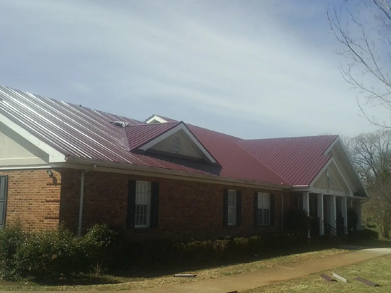 Red metal roof with gabled entries on a long brick building, from a Hail Damage Roof Repair job in Van Etten