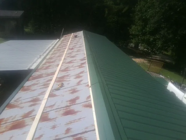 Old rusted panels beside newly installed green metal roofing — Wind Damage Roof Repair by Roofing Brothers in Van Etten