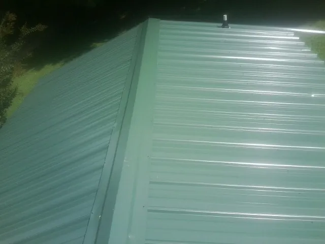 New green metal panels meeting at the ridge of a roof — Flat Roof Repair work by our crew in Van Etten