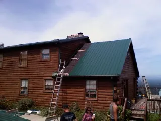 Green metal roof going on a two story log home with ladders set in Van Etten