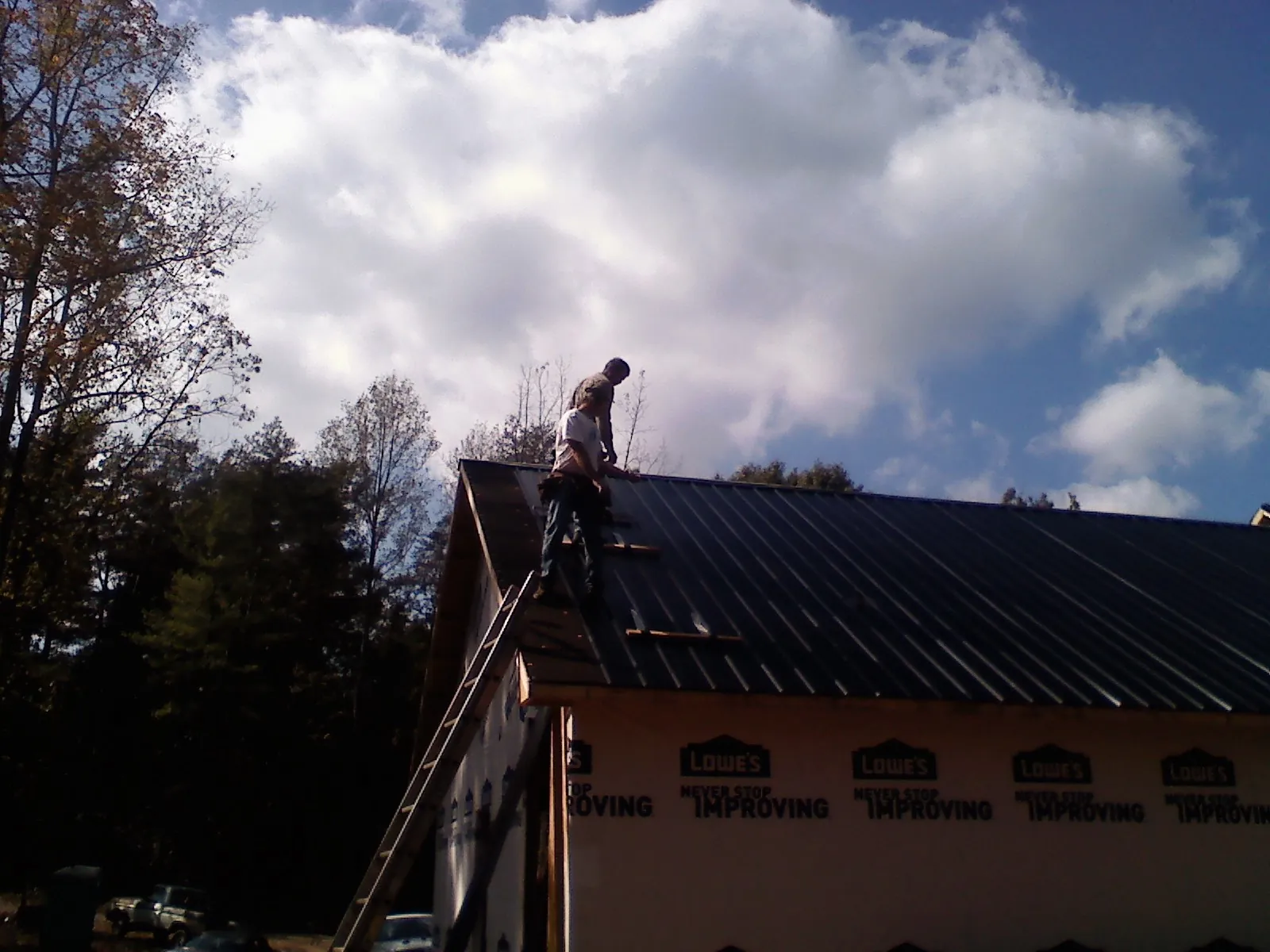 Roofer fastening dark metal panels high against a cloudy sky, from a Roof Inspection job in Van Etten