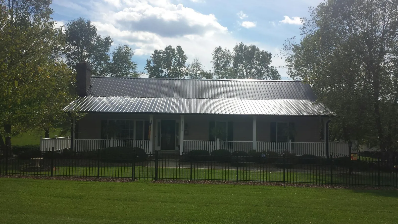 Gray metal roof on a brick ranch with a full width front porch — Gutter Guard Installation work by our crew in Van Etten