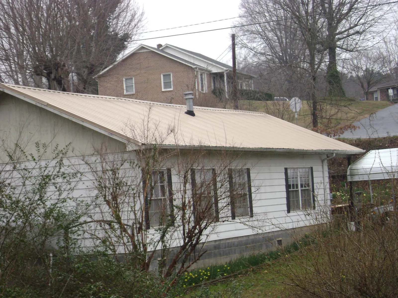 Tan metal roof on a white sided house set into a hillside — Commercial Roofing by Roofing Brothers in Van Etten